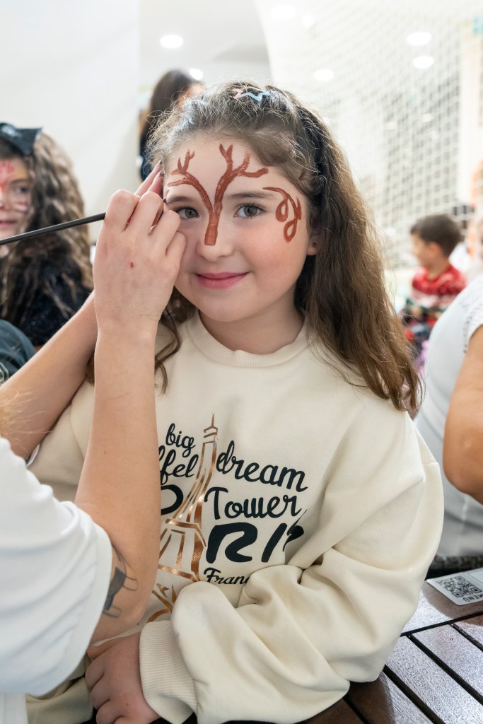 Yüz boyama etkinliğinde bir çocuğun yüzü renkli desenlerle boyanıyor.