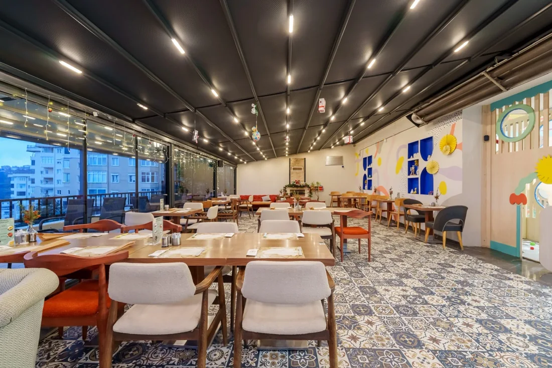 Filifu'nun kafe bölümünde ahşap masalar, krem ve turuncu sandalyeler, geniş camlar ve desenli karo zemin.