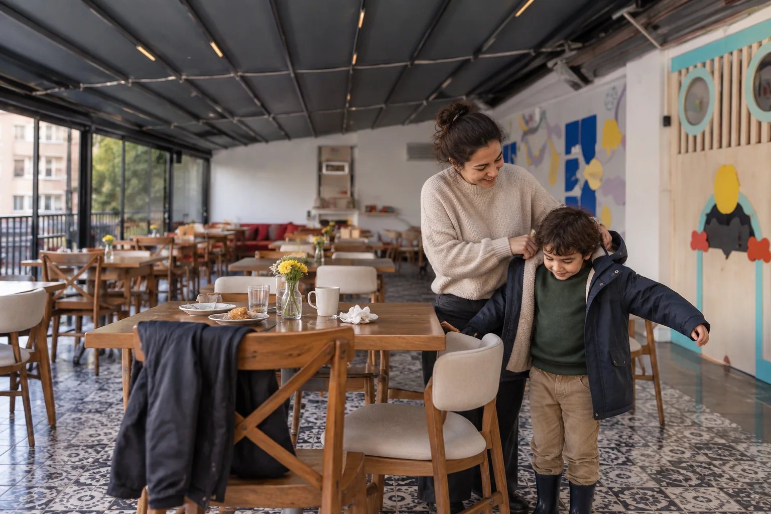 Kafe masasının yanında çocuğuna montunu giydiren ebeveyn