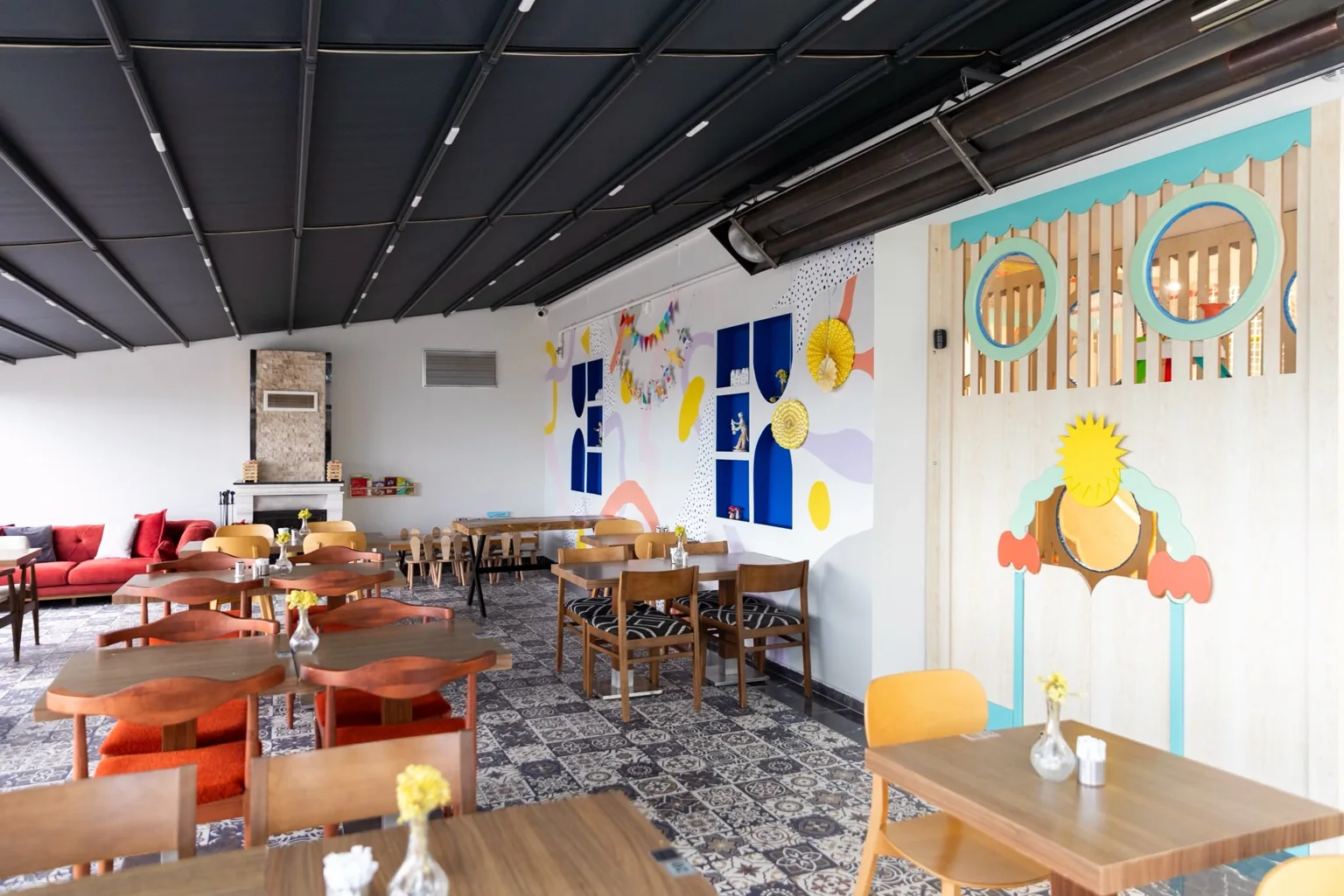 Tables en bois et chaises colorées devant un mur pastel et un sol à motifs