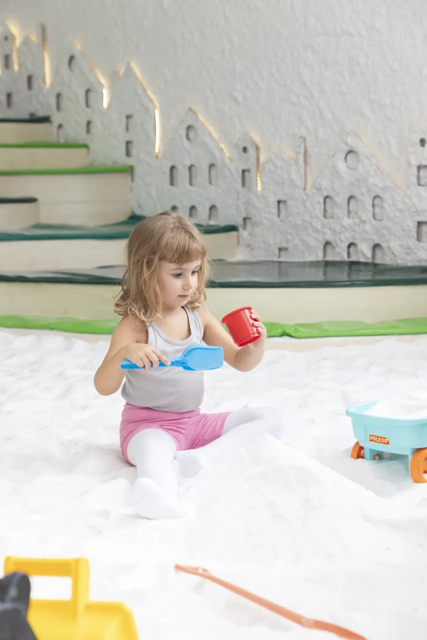 A child holding a blue toy shovel and a red cup on the white salt floor at Filifu