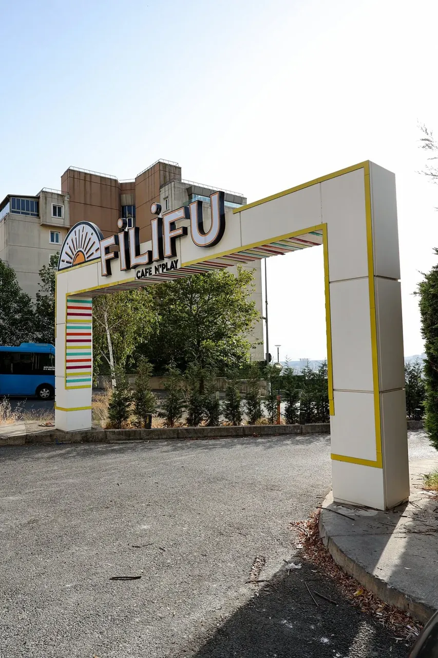 Vue de côté de l’enseigne Filifu Cafe N’Play sur son cadre blanc et jaune