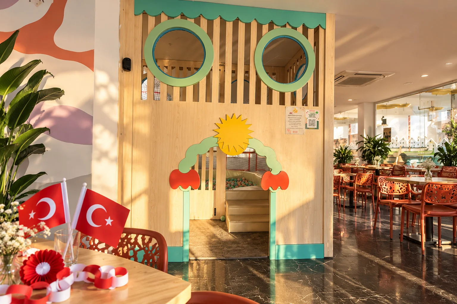 Filifu’nun güneş figürlü ahşap oyun girişi önünde Türk bayrakları ve kırmızı beyaz kâğıt süsler
